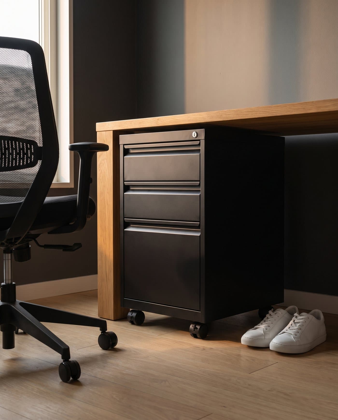 Le caisson Loot glissé sous un bureau en chêne, à côté du piètement d'une chaise