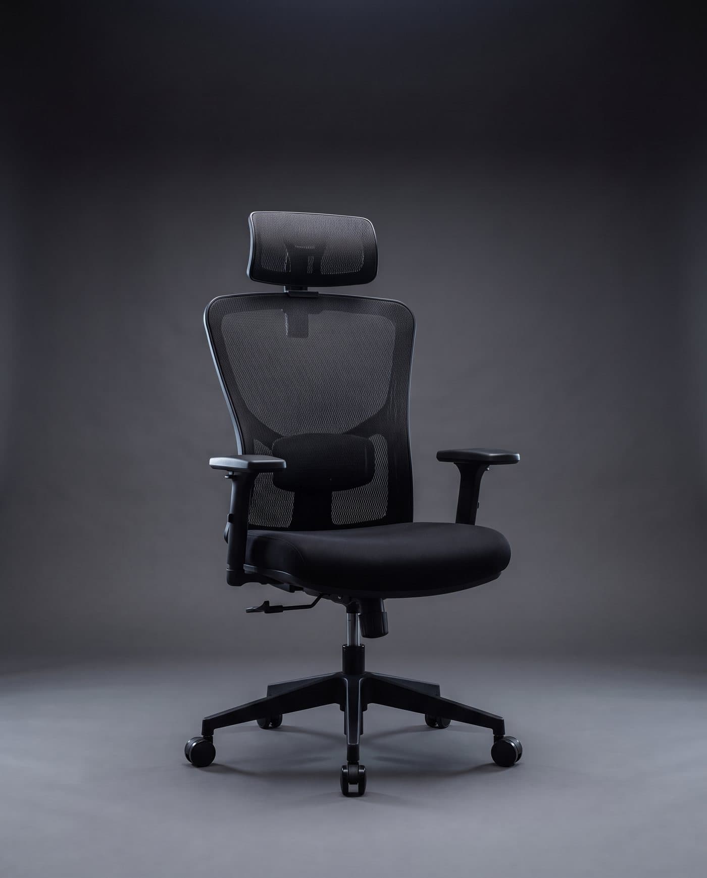 Chaise ergonomique en maille noire avec appui-tête et accoudoirs réglables, sur fond anthracite