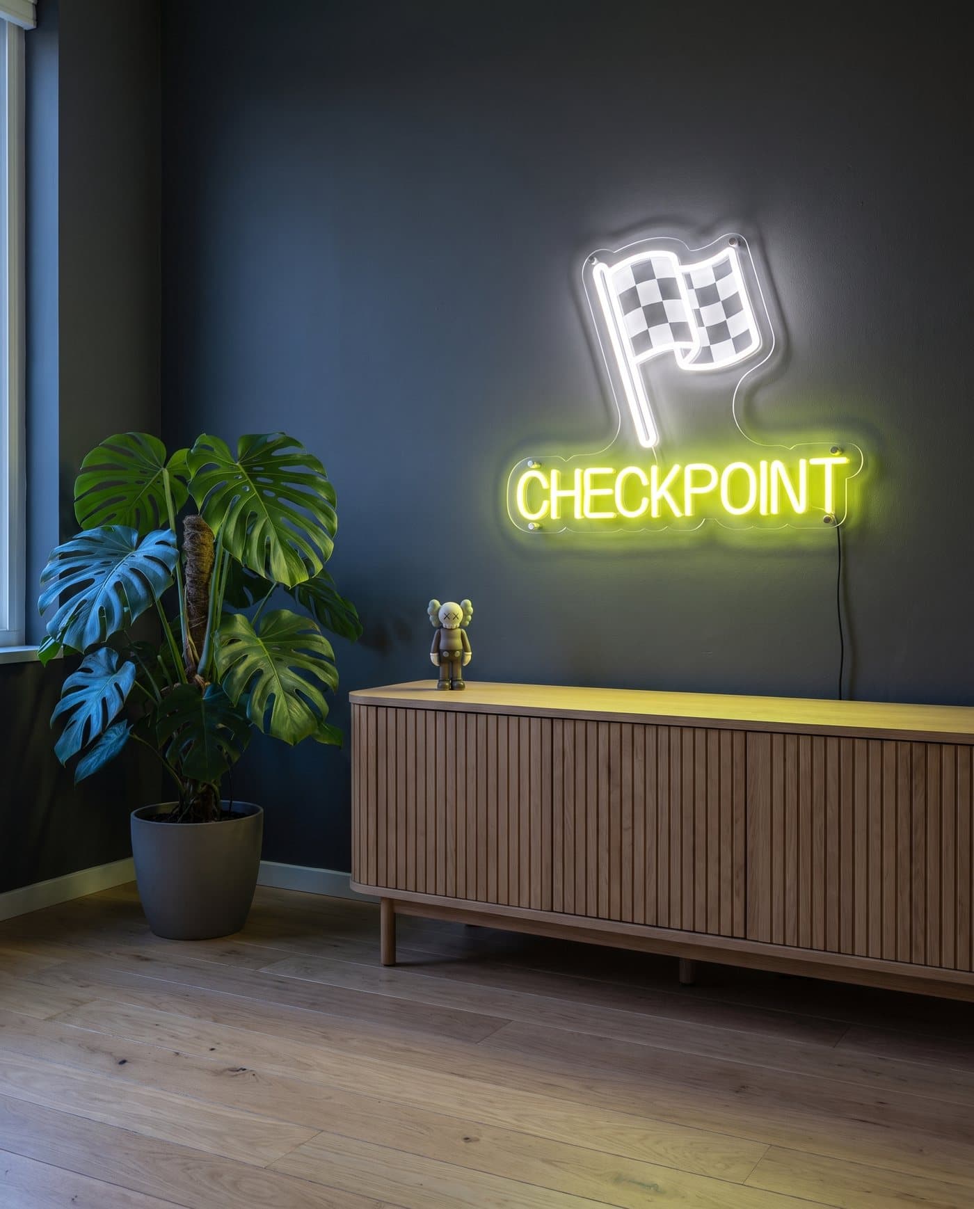 Le néon Checkpoint allumé au-dessus d'un meuble bas en chêne, à côté d'une grande plante