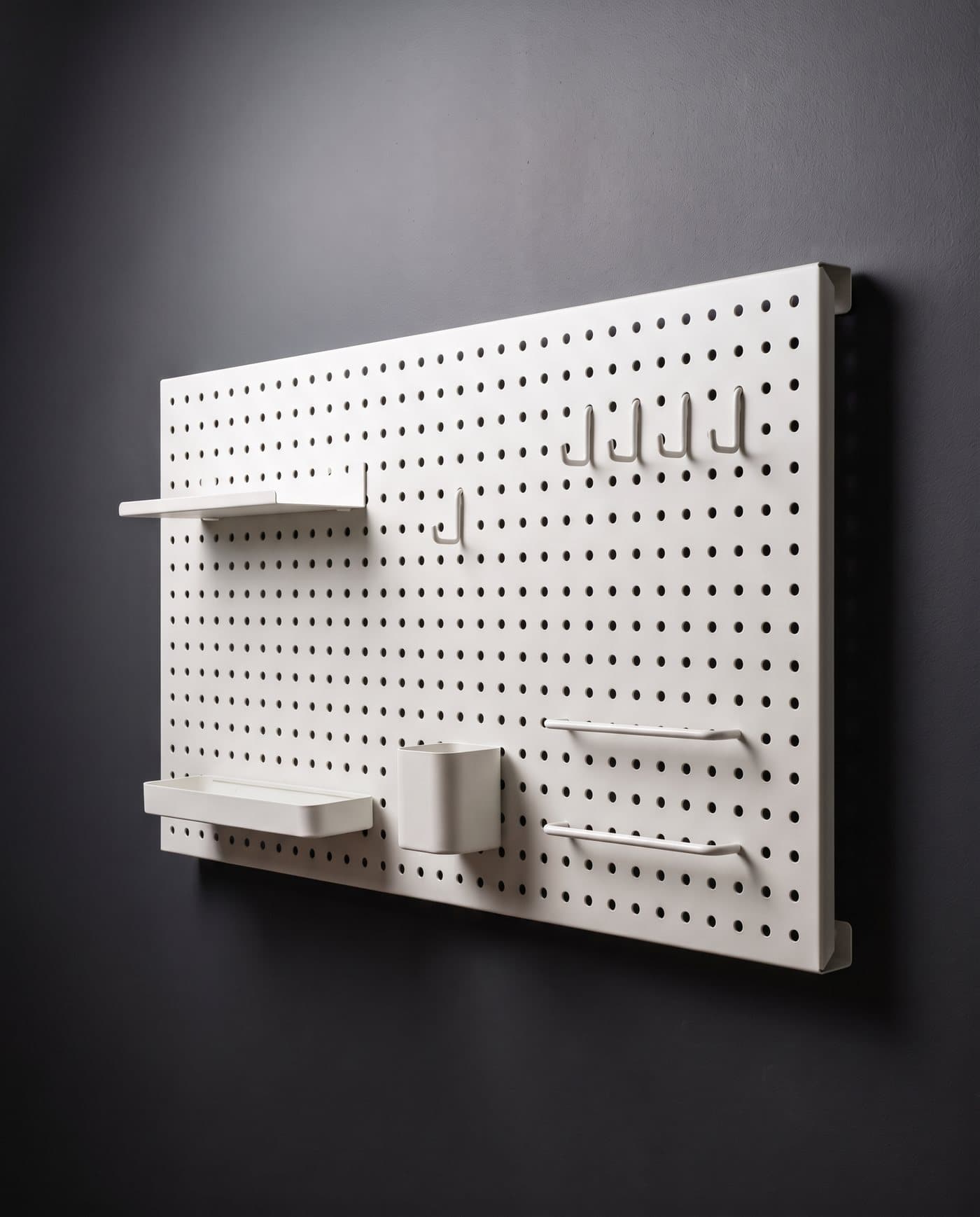 Panneau perforé en acier blanc avec tablettes, bac, pot et crochets blancs, fixé sur un mur anthracite